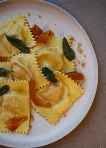 Hausgemachte Ravioli mit cremiger Kürbis-Taleggio-Füllung, Nussbutter, Salbei, gepickeltem Kürbis und Amarettini. Ein herbstliches Pasta-Rezept mit besonderem Twist.