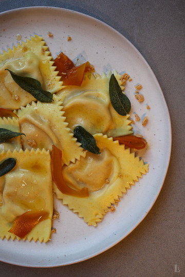 Hausgemachte Ravioli mit cremiger Kürbis-Taleggio-Füllung, Nussbutter, Salbei, gepickeltem Kürbis und Amarettini. Ein herbstliches Pasta-Rezept mit besonderem Twist.